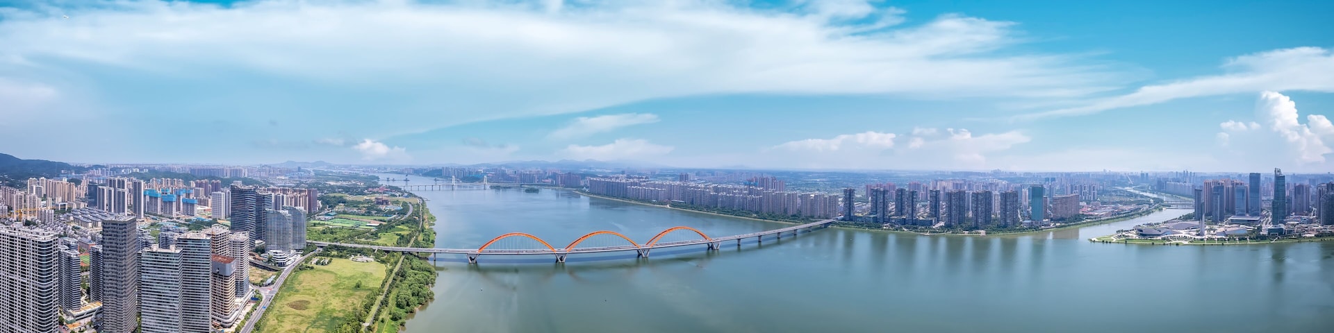 A river with a bridge, a cityscape with high-rise buildings, and a clear blue sky.
