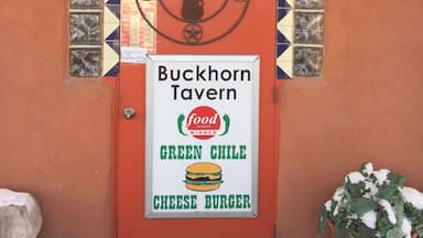 Uma porta vermelha com uma placa de 'Welcome' e uma placa 'Buckhorn Tavern' anunciando um hambúrguer de queijo com chile verde.