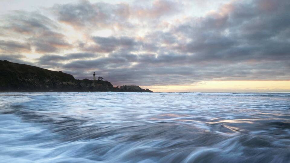 A coastal landscape with a lighthouse on a cliff, calm sea, and a cloudy sky.