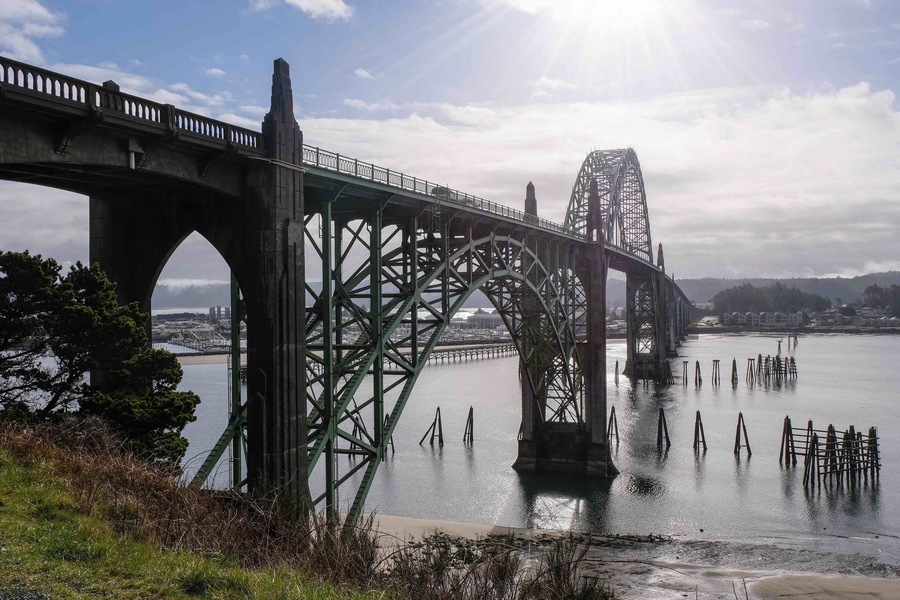 Un gran puente de acero que cruza un río, con un paisaje urbano al fondo.