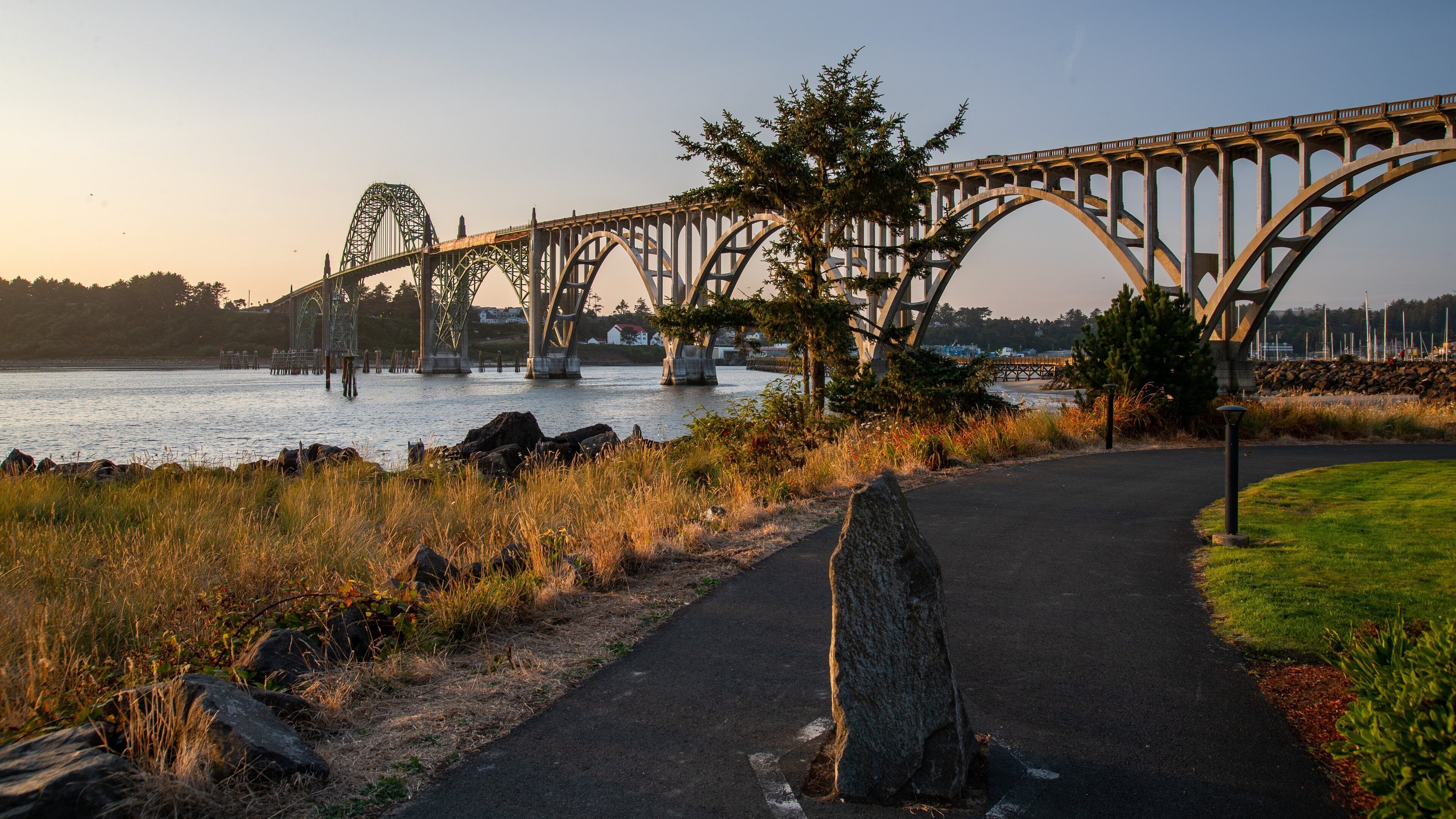 A steel bridge over a river with a walking path beside it.
