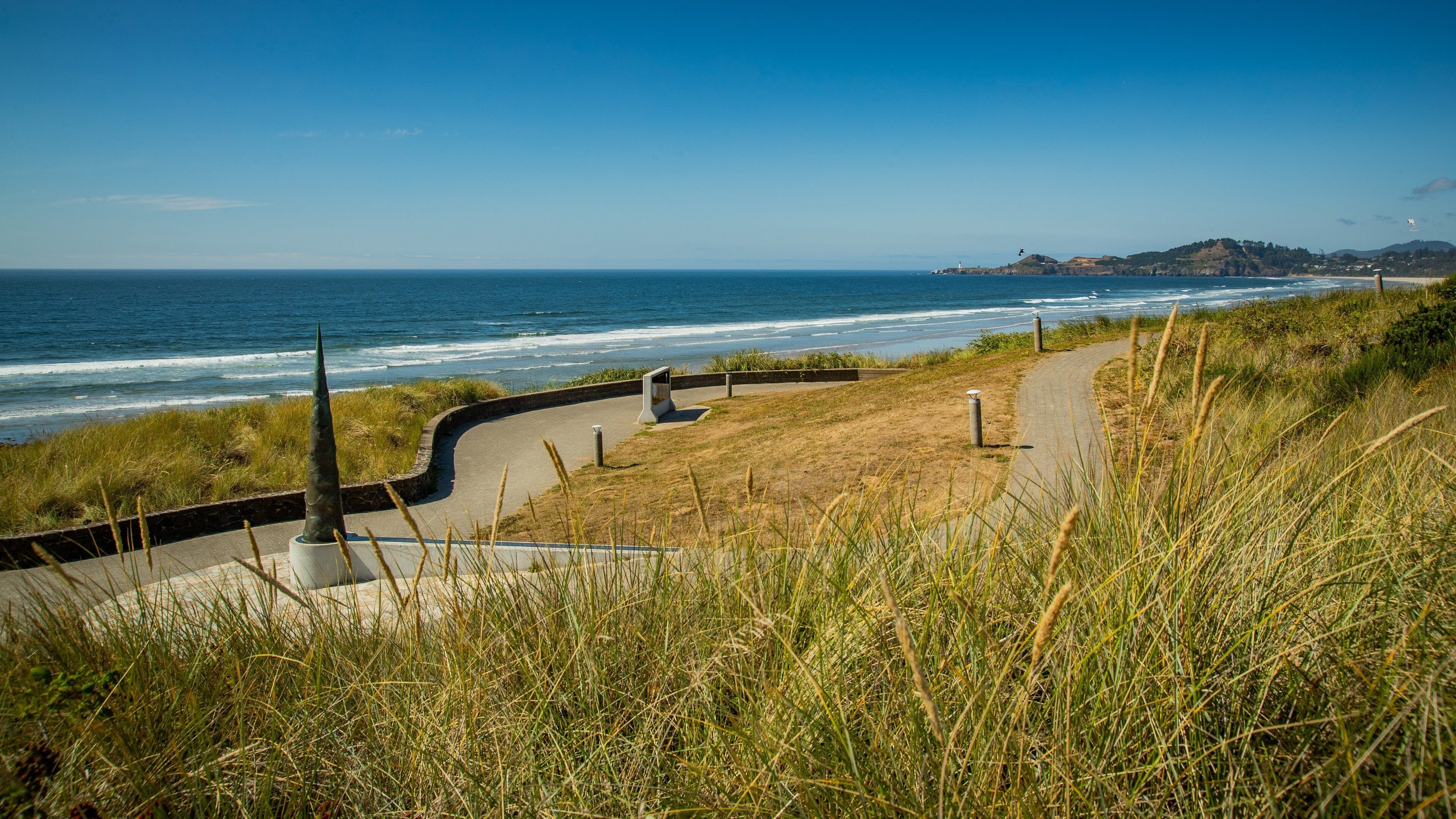 A coastal pathway with grass, a lighthouse, and the ocean.