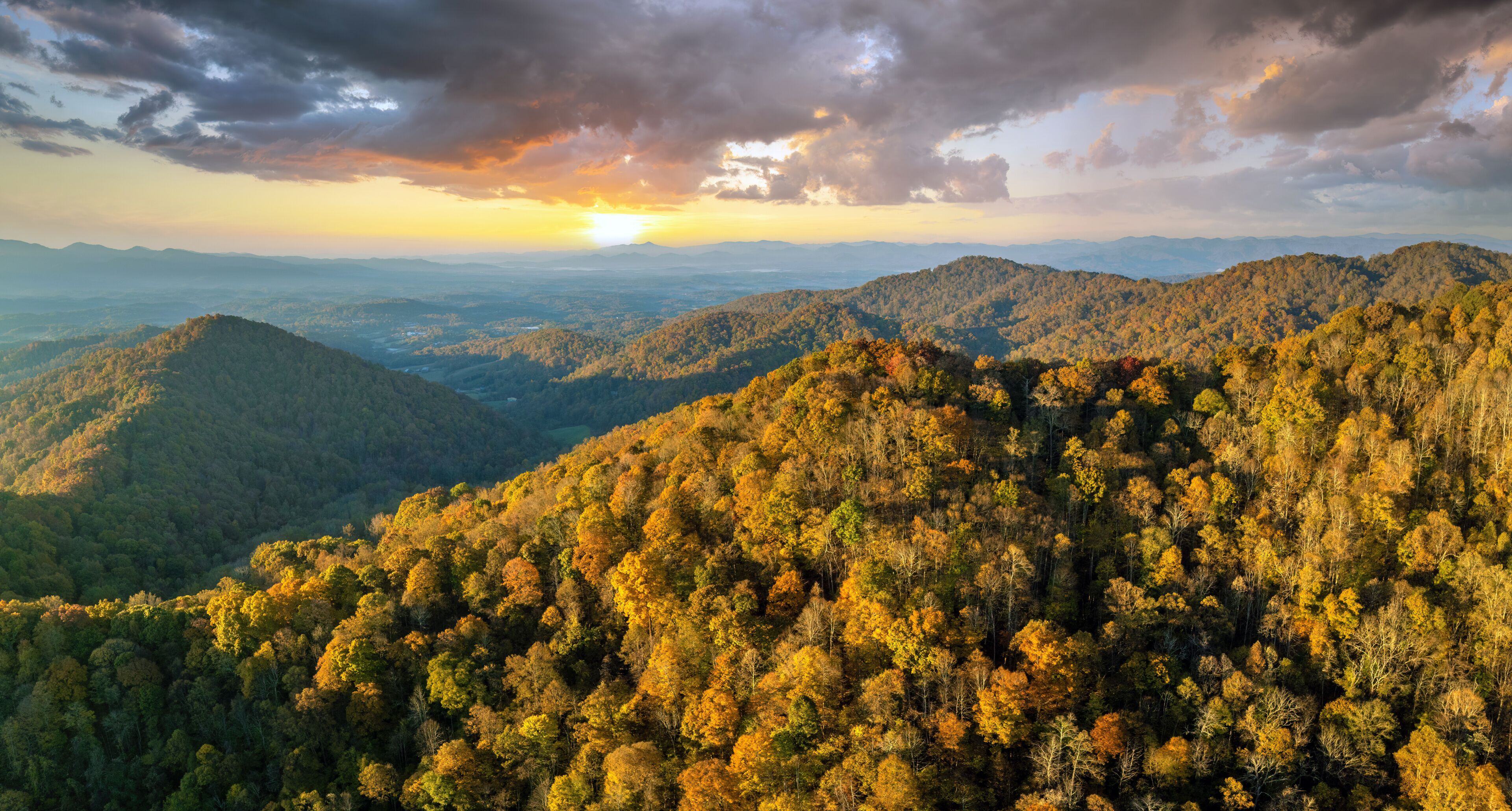 A mountainous landscape with dense forests and a sunset in the background.