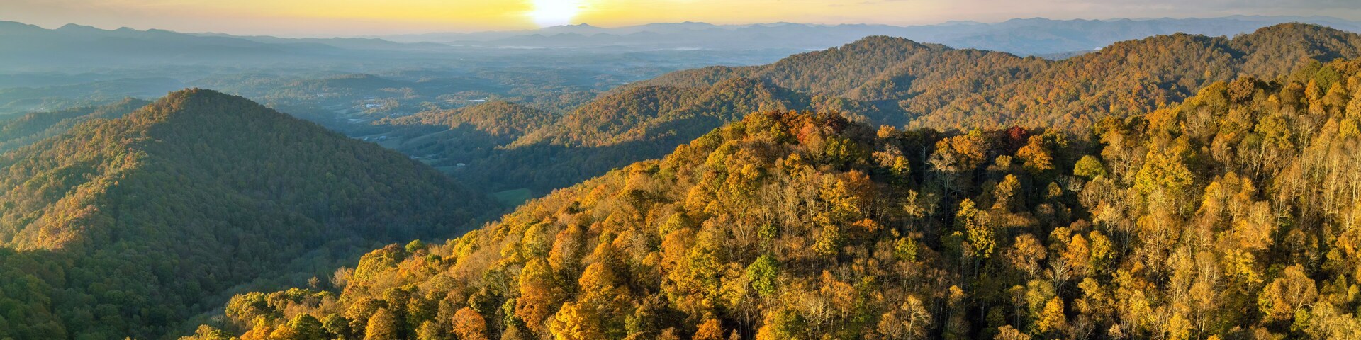 A mountainous landscape with dense forests and a sunset in the background.
