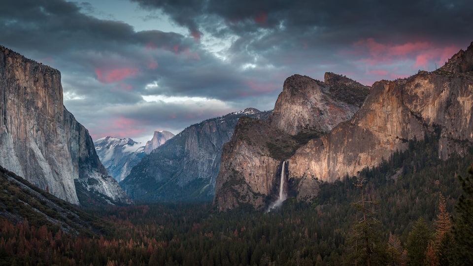 A canyon with a waterfall, steep cliffs, and a forested valley.