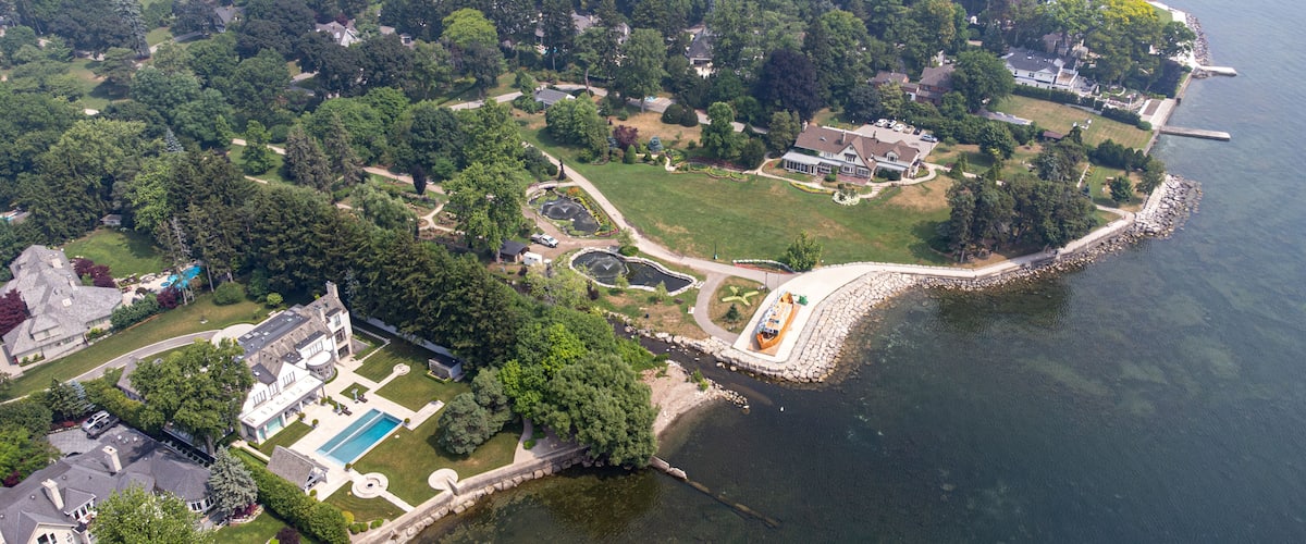 An aerial view of a coastal residential area with houses, a large swimming pool, and a rocky shoreline.