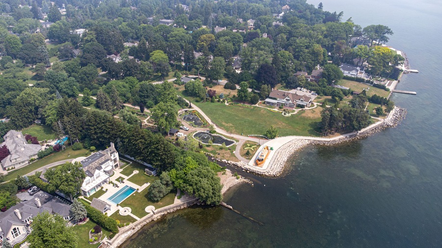 Vue aérienne d’un quartier résidentiel situé sur la côte, avec des maisons, une grande piscine et une côte rocheuse.