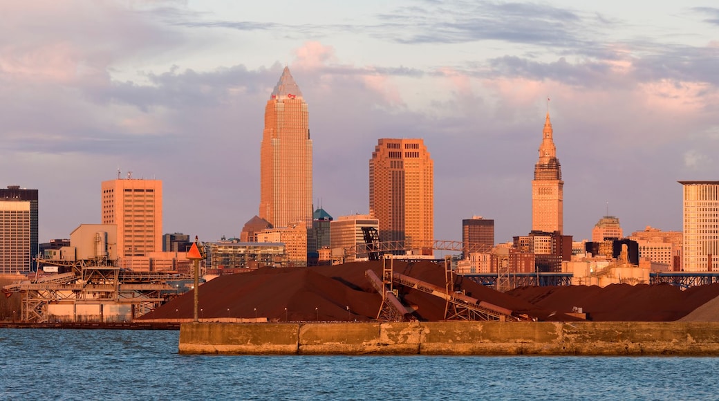 A city skyline with prominent skyscrapers, including a tall, pointed building and a cylindrical tower, across a body of water.