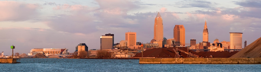 A city skyline with prominent skyscrapers, including a tall, pointed building and a cylindrical tower, across a body of water.