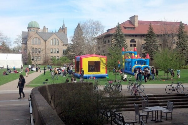 A university campus with a large green lawn, a bounce house, and a castle-themed play structure.