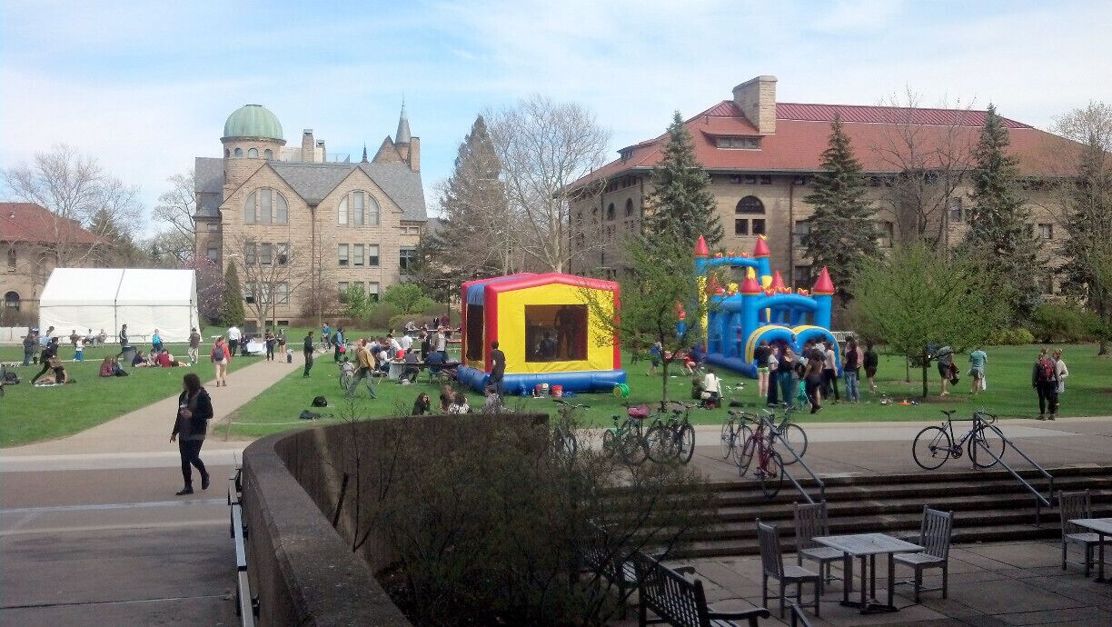 A university campus with a large green lawn, a bounce house, and a castle-themed play structure.