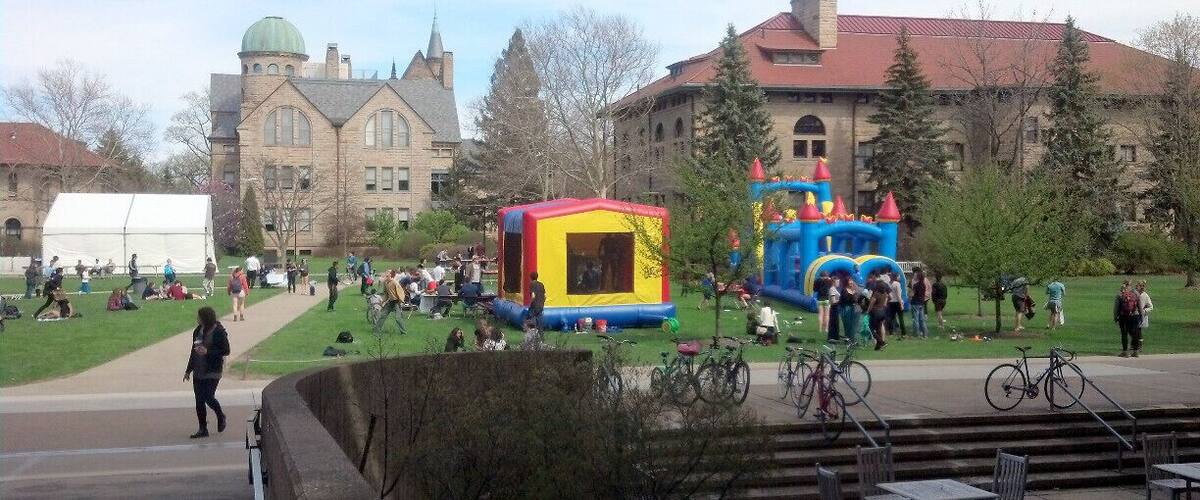 A university campus with a large green lawn, a bounce house, and a castle-themed play structure.