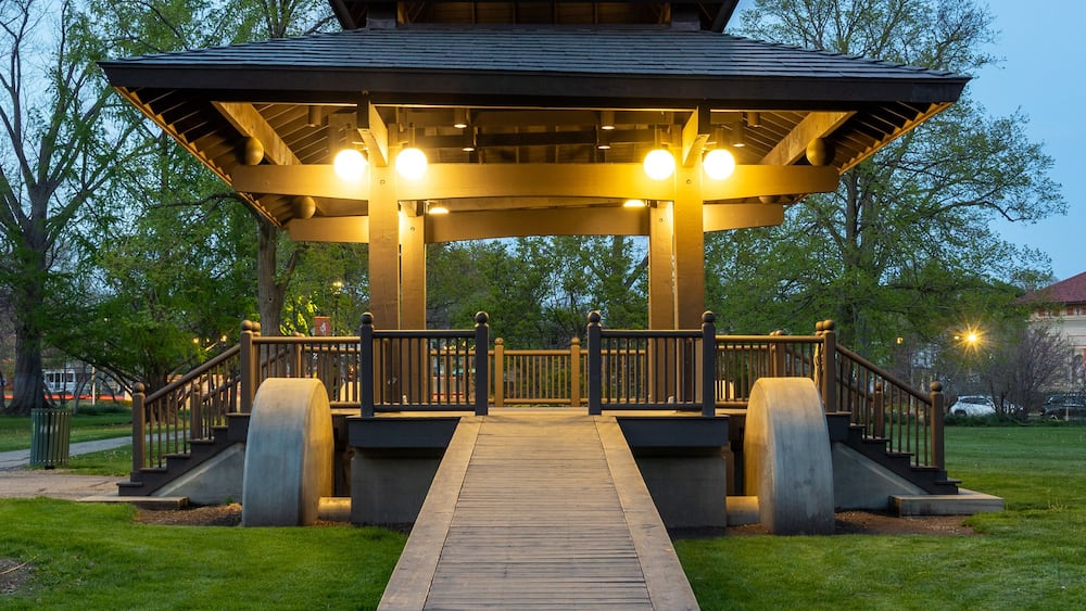 A gazebo with a wooden roof and a metal railing, surrounded by a grassy area with trees.
