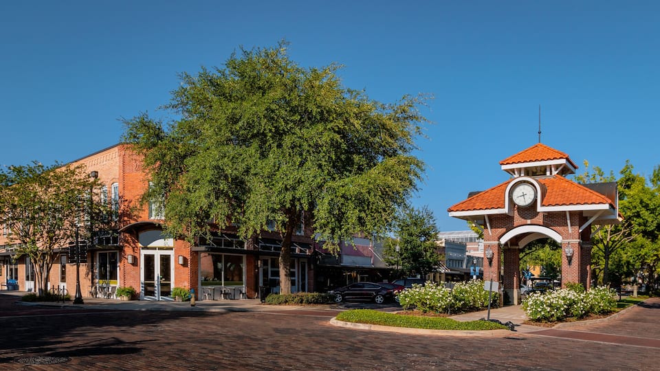 A street with a clock tower, brick buildings, and trees.