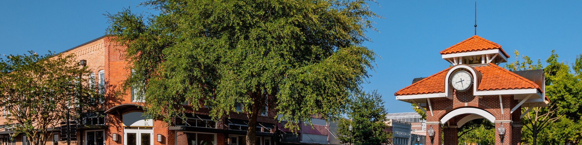 A street with a clock tower, brick buildings, and trees.