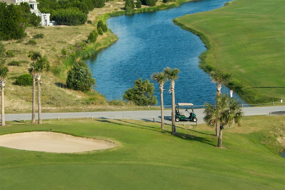 Um campo de golfe com um corpo de água e casas ao fundo.