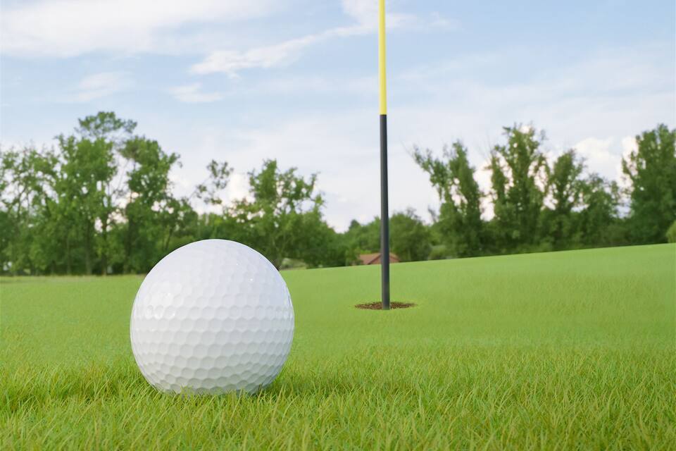 A golf ball on a green field with a flagpole and a flag.