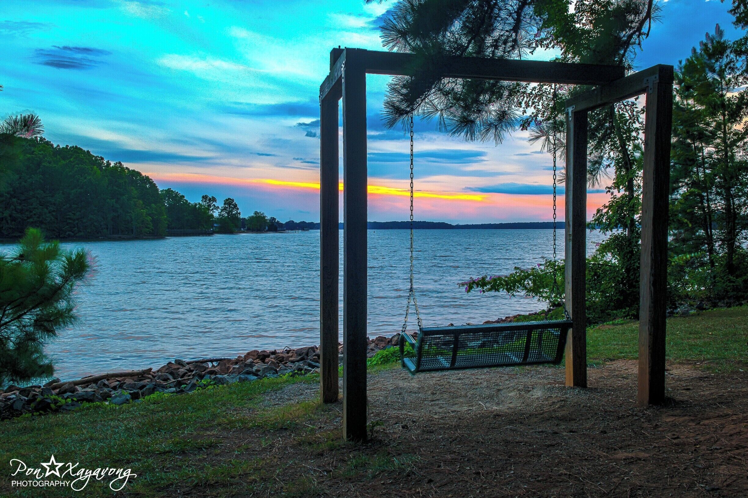 A wooden swing set by a lakeside at sunset.
