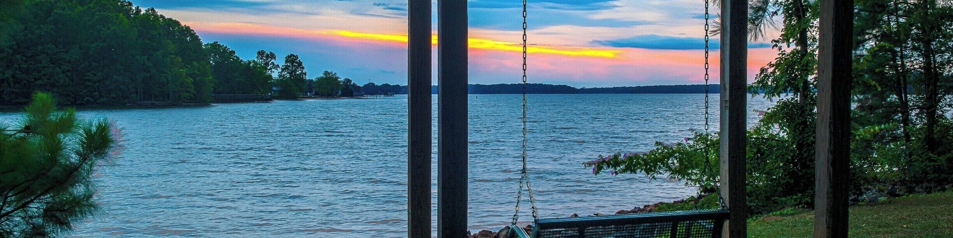 Un columpio de madera junto a un lago al atardecer.