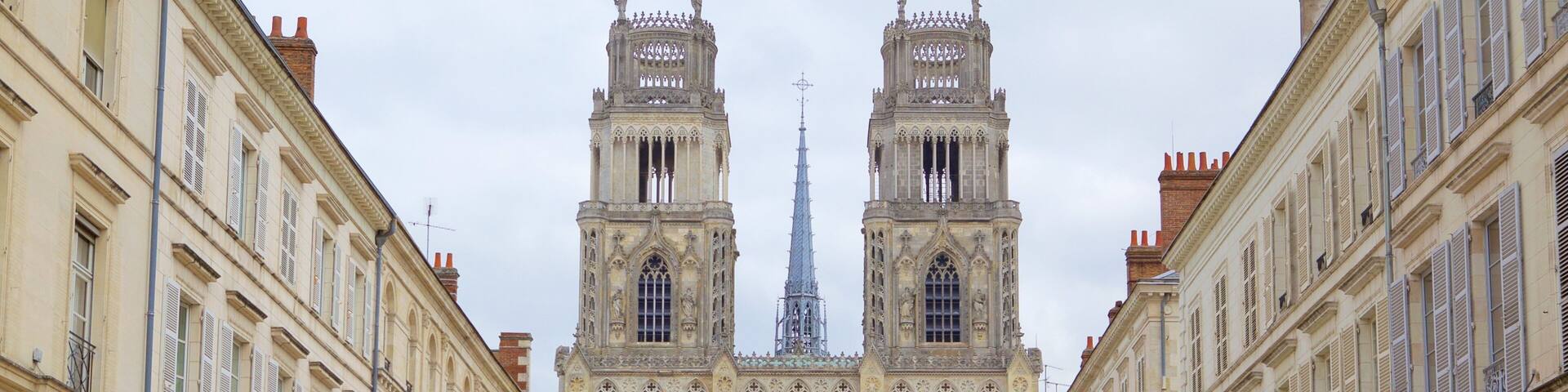 A grand cathedral with twin towers and a spire, flanked by ornate buildings and a central green space.