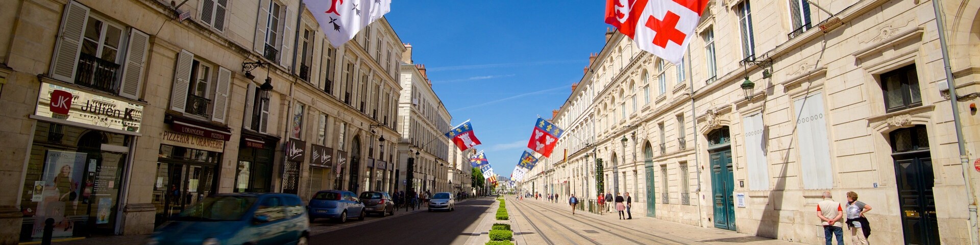 A street lined with historic buildings, flags, and a tram track.