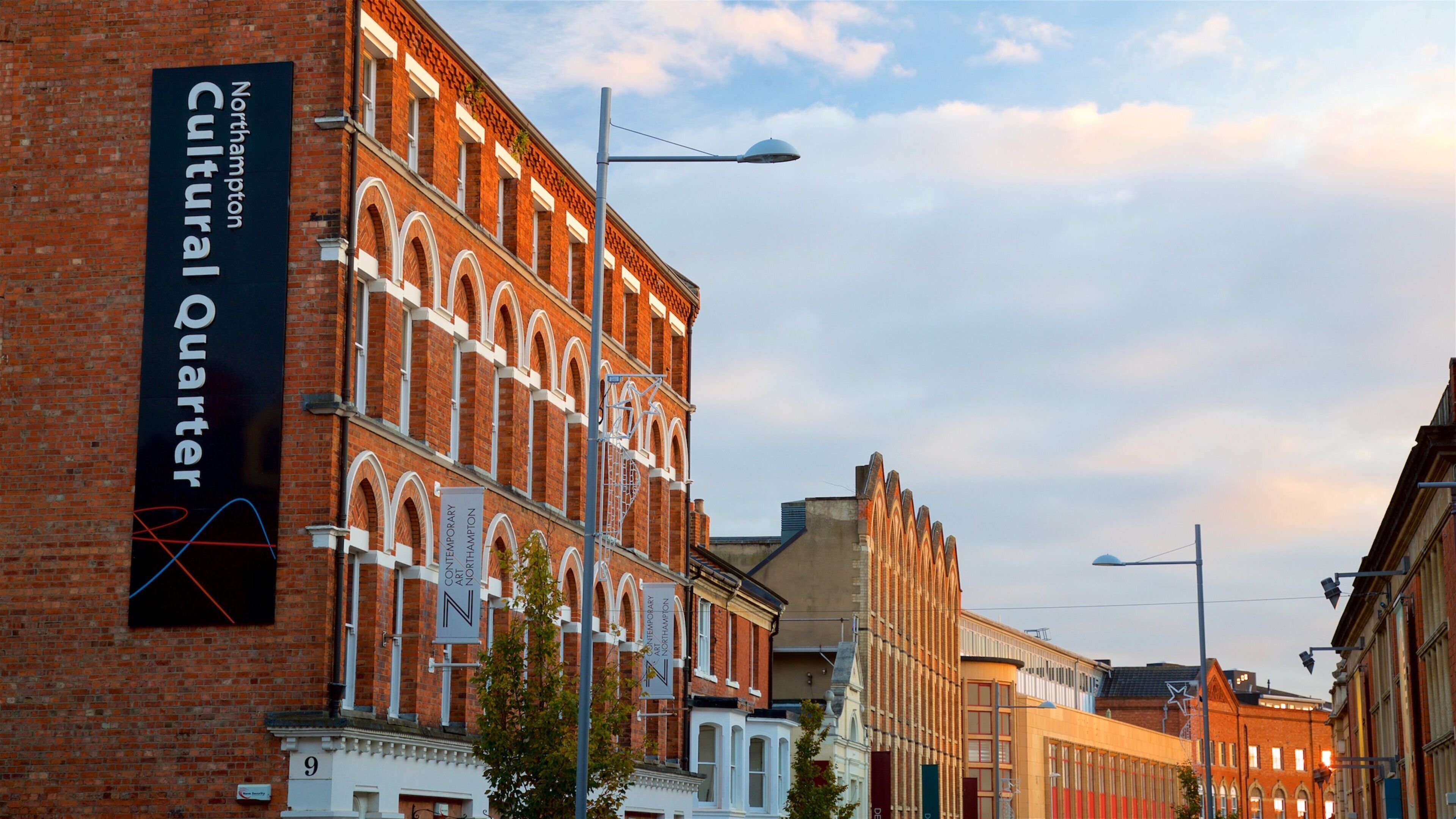 A street with red brick buildings, a sign for Northampton Cultural Quarter, and street lamps.