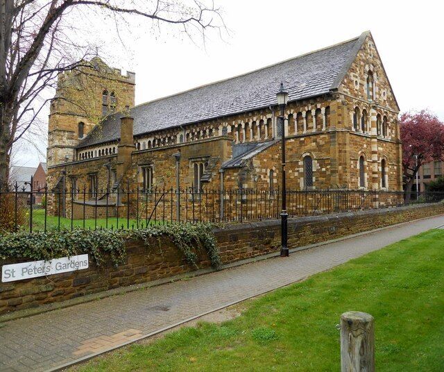 A historic stone building with a tower, a paved pathway, and a sign reading "St. Peter's Gardens".