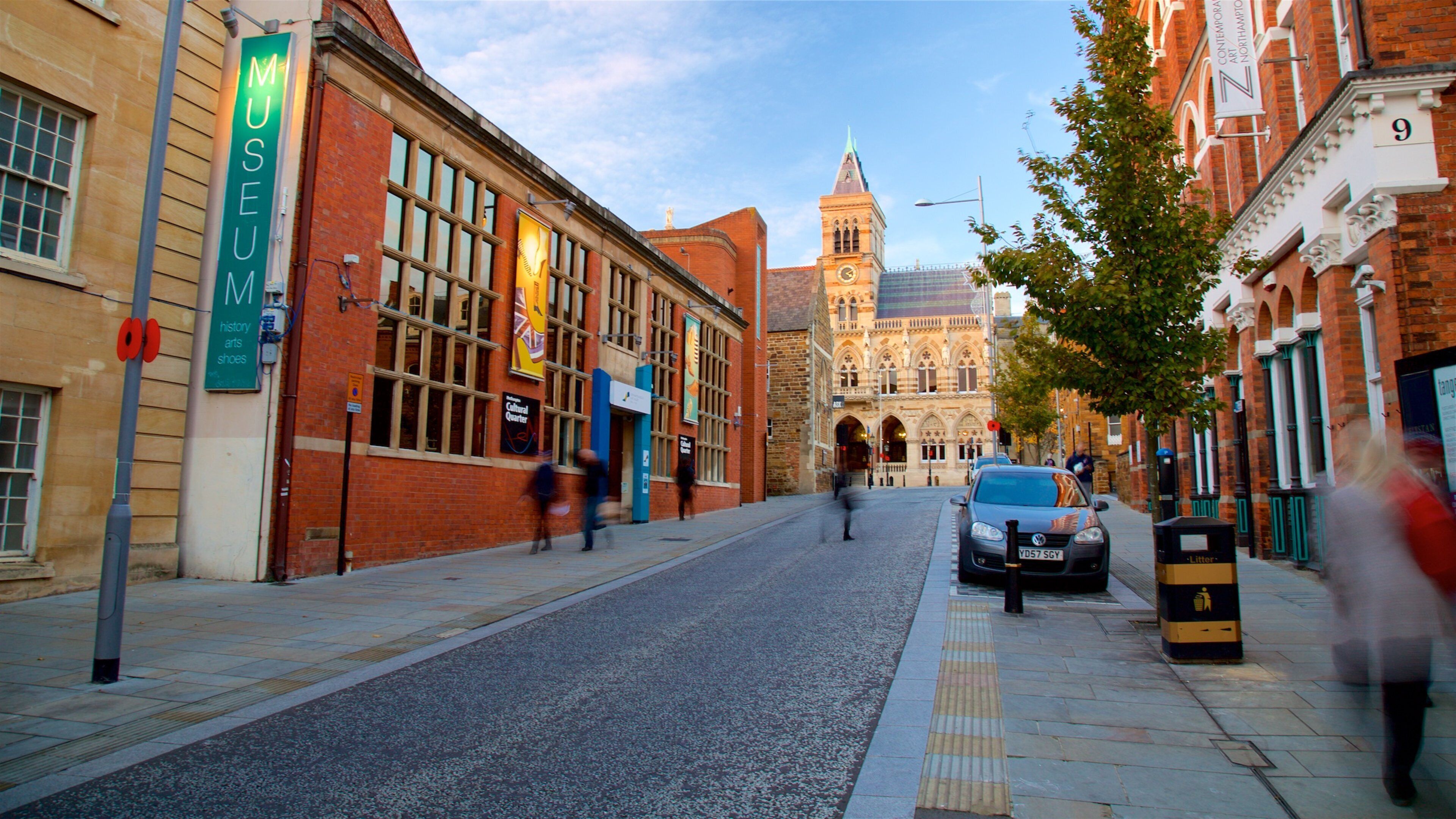 A street with a museum sign, a clock tower, and a car parked on the side.