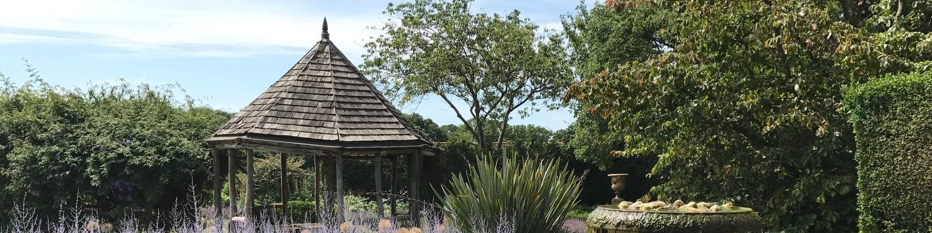 A garden with a gazebo, a fountain, and lavender bushes.