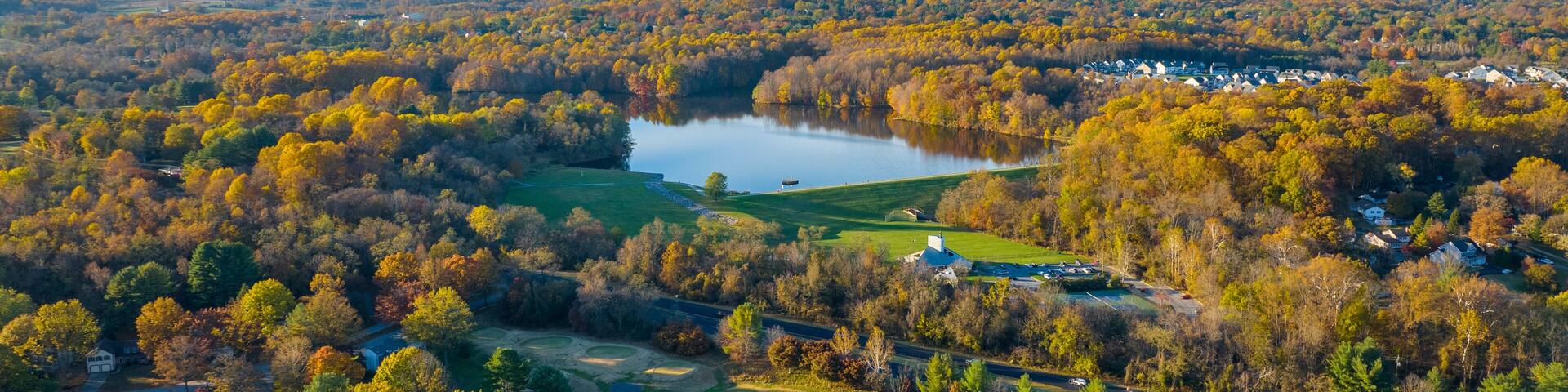 A golf course with a lake and autumn-colored trees.