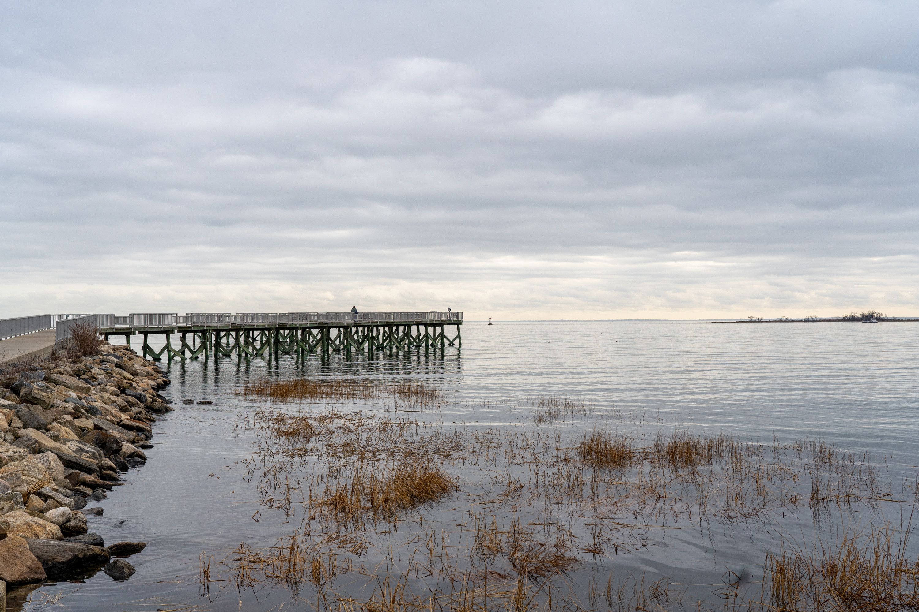A pier extending into calm waters with overcast skies.