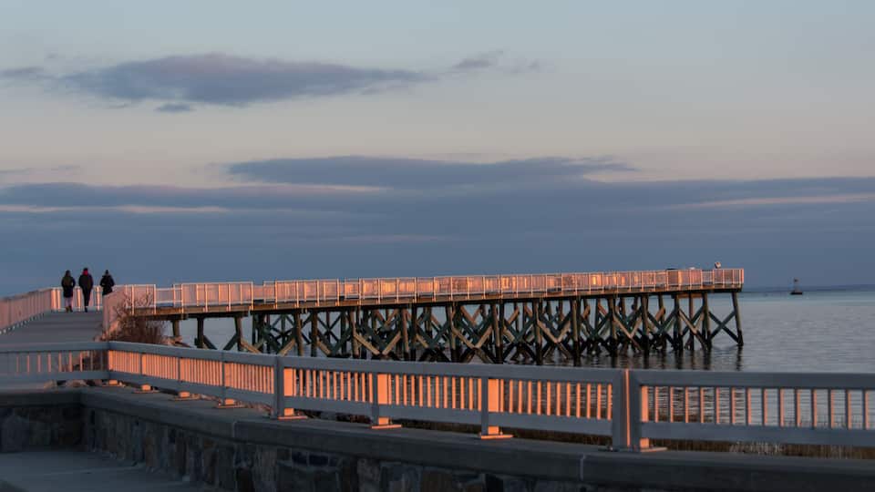 A pier extending into calm waters at dusk with a stone walkway and railings.