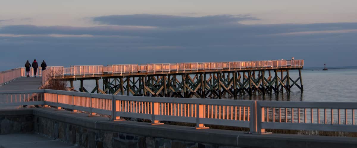 A pier extending into calm waters at dusk with a stone walkway and railings.