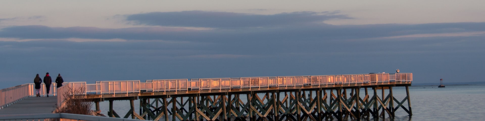 A pier extending into calm waters at dusk with a stone walkway and railings.