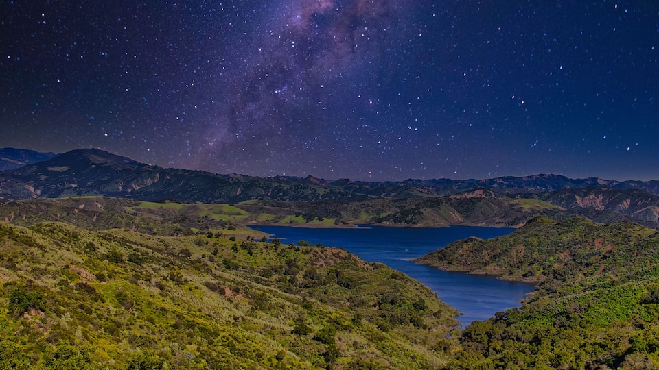 A starry night sky over a mountainous landscape with a lake.