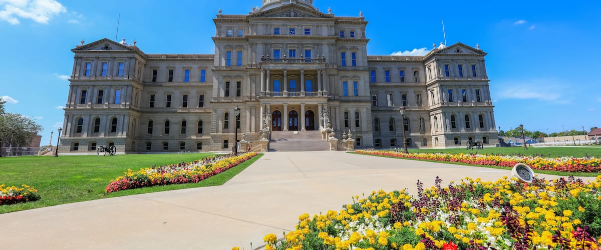 A large neoclassical building with a prominent dome and columns, surrounded by a well-maintained garden with colorful flowers.