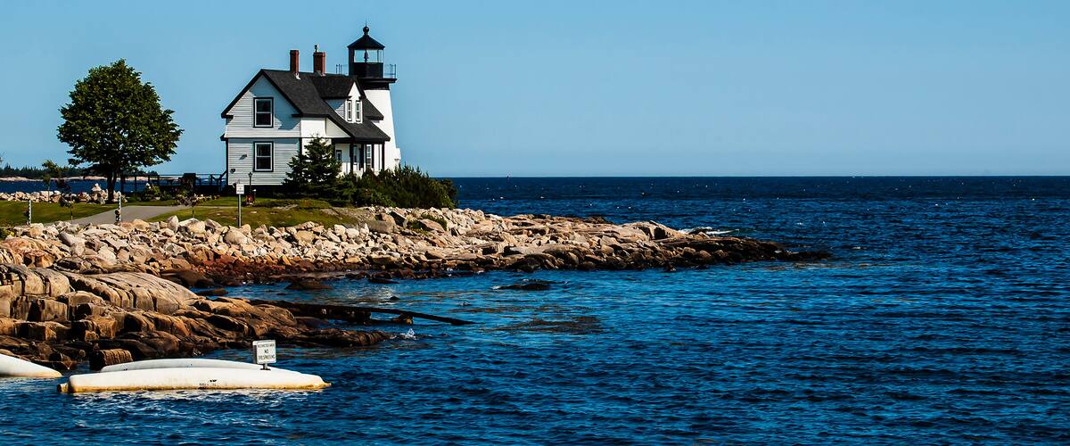 A lighthouse on a rocky shore with a clear blue sky.