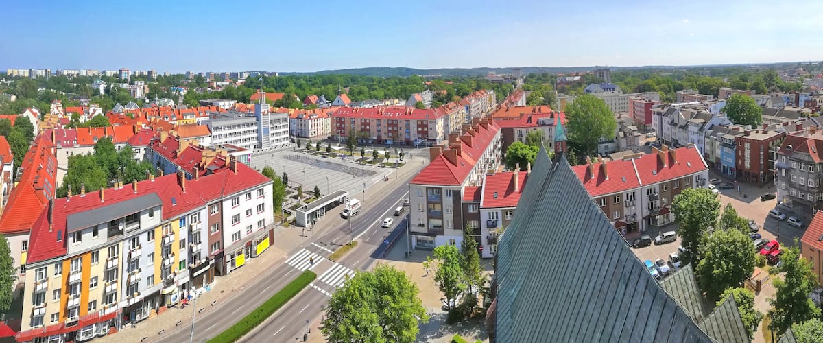 A cityscape with red-roofed buildings, a prominent church spire, and a wide street.