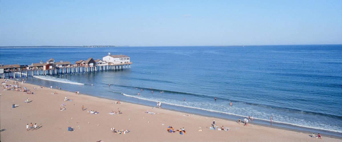 A beach with a pier extending into the ocean, people sunbathing, and a clear blue sky.