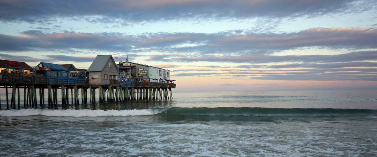 A pier extending into the ocean with buildings on it and waves crashing against the shore.