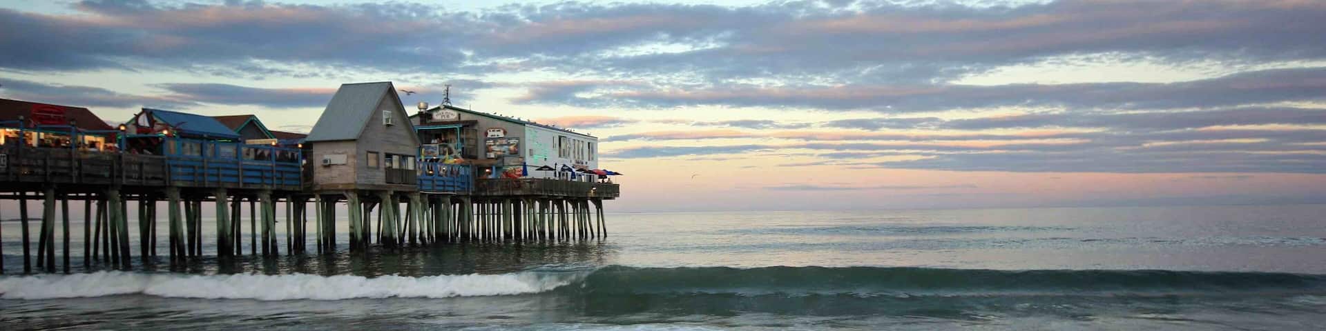 A pier extending into the ocean with buildings on it and waves crashing against the shore.