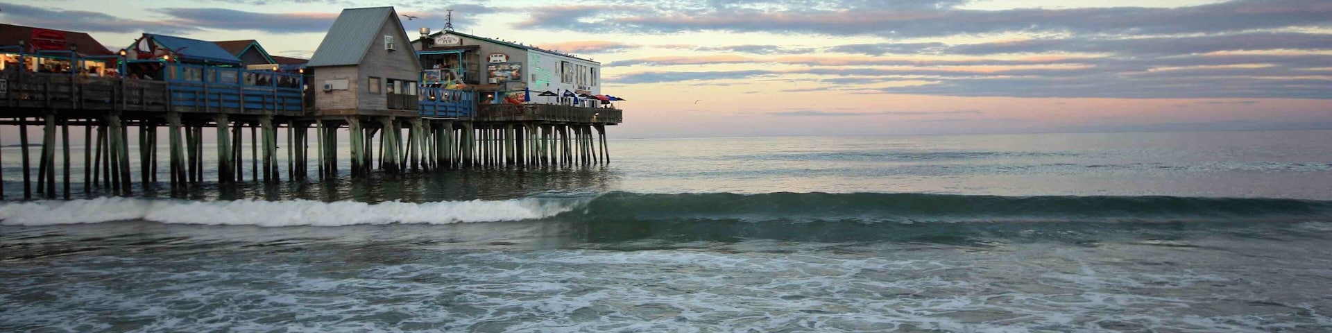 Un muelle que se adentra en el océano, con edificios construidos sobre él y olas rompiendo en la orilla.