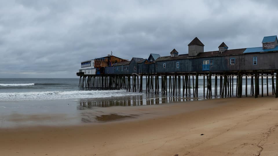 A coastal pier with wooden structures extending into the sea under a cloudy sky.