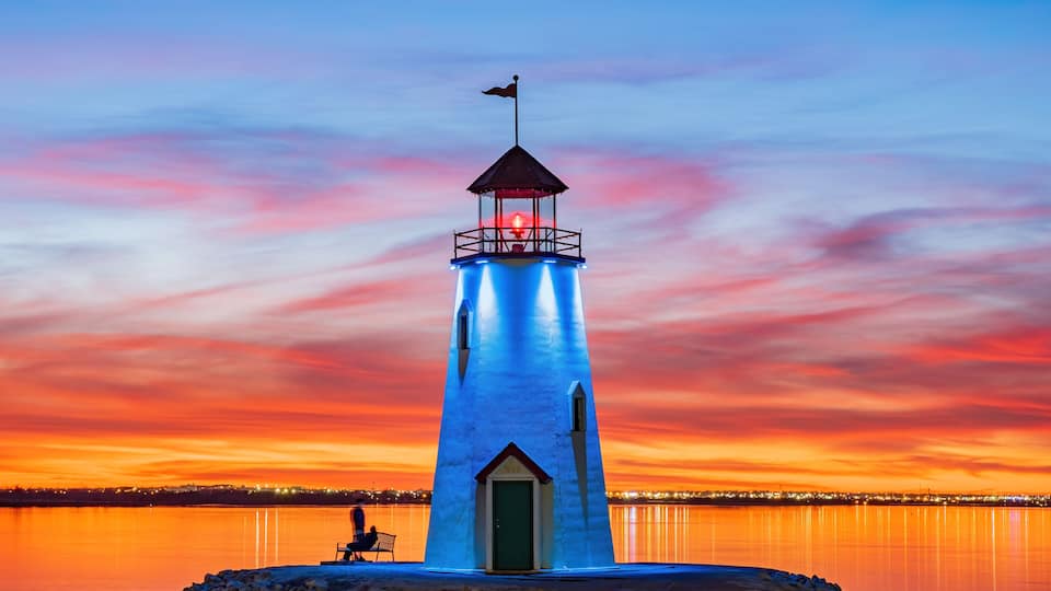 A lighthouse at sunset with a clear sky and calm water.