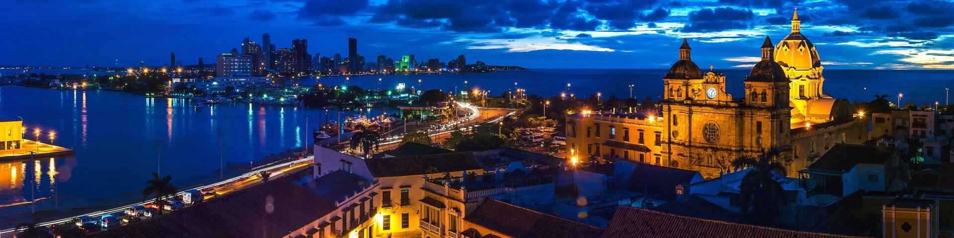 A coastal cityscape at night with a prominent cathedral and a modern skyline.