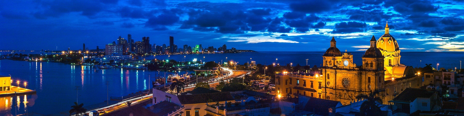 Uma paisagem urbana costeira noturna, com uma catedral imponente e um horizonte moderno.