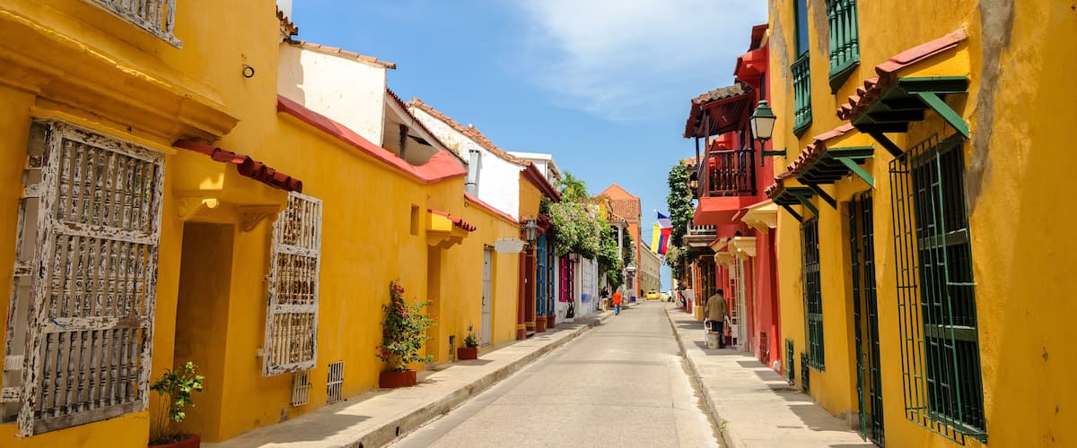 A narrow street lined with colorful buildings, featuring balconies and potted plants.