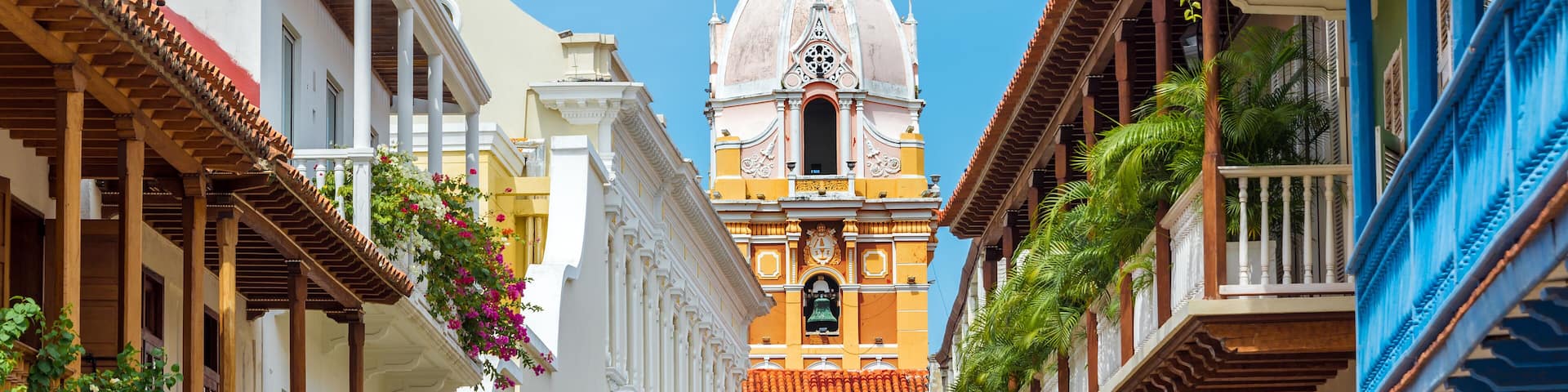 A street with colorful buildings, a bell tower, and balconies with flowers.
