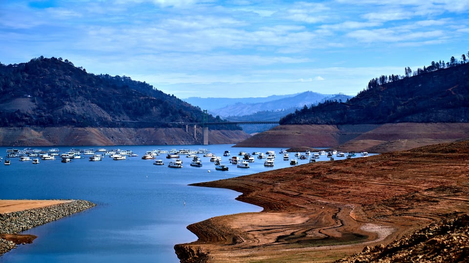 A lake with boats, a bridge, and hilly terrain.