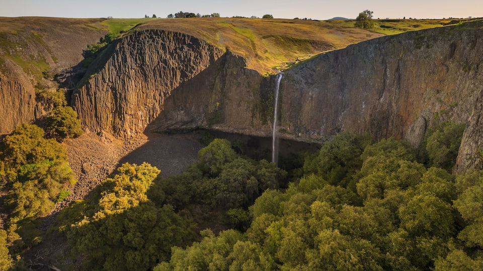 A waterfall cascading down a steep cliff surrounded by dense forest.